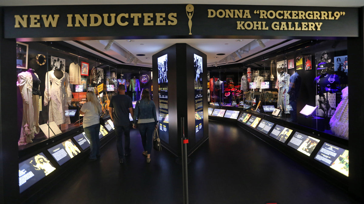 Visitors in the New Inductees gallery at the Rock & Roll Hall of Fame, with a rail of small screens along the cases