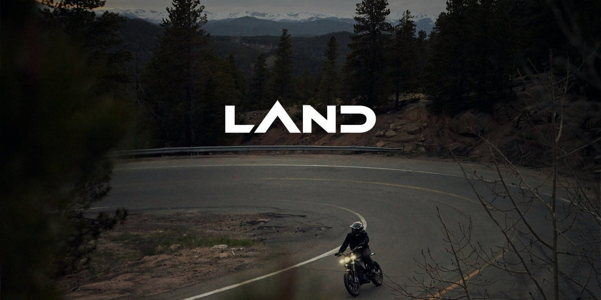 A rider on a LAND District takes a mountain switchback at dusk with the headlight on, under the LAND logo